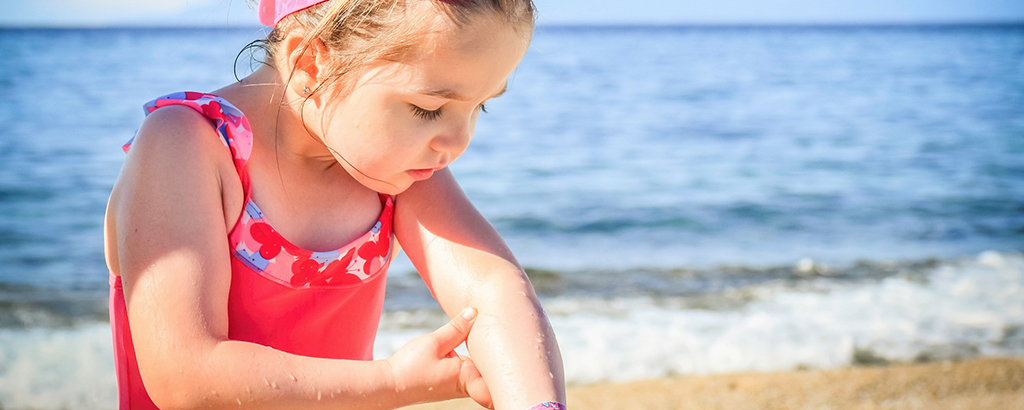 niña con traje de baño rojo mirandose el brazo con el mar de fondo