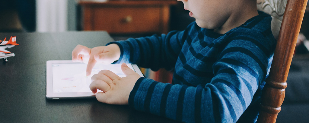 niño jugando con una tablet sentado en una silla de madera